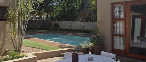 Un patio trasero con piscina, mesa y sillas.