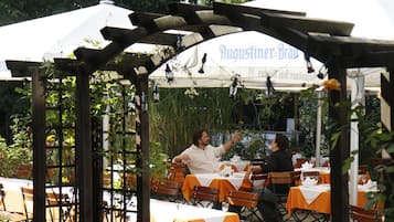 Area esterna con tavoli e sedie, coperta da una tettoia con la scritta 'Augustiner-Brau'.