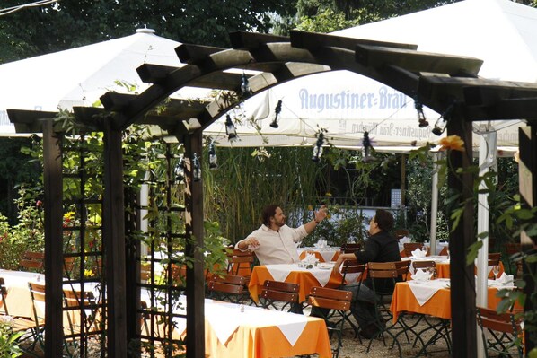 Un área de comedor al aire libre con mesas y sillas bajo una marquesina con el nombre 'Augustiner-Brau'.