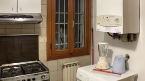 A compact kitchen with a gas stove, a built-in oven, a washing machine, and a window with wooden frames. - Admiral Home (Venice)