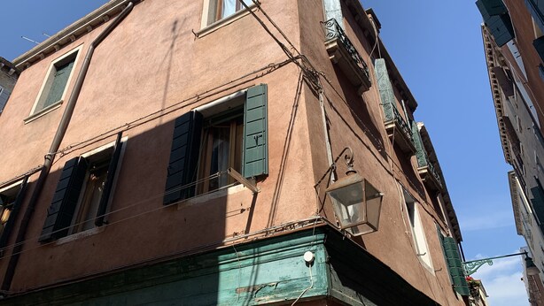 A corner of a building with a pink facade, green shutters, and a visible 'T' on the window. - Admiral Home (Venice)