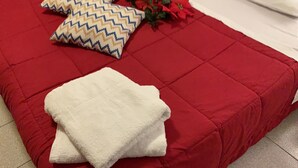A hotel room with a red bedspread, two pillows with a zigzag pattern, a white towel, and a bouquet of red flowers. - Admiral Home (Venice)