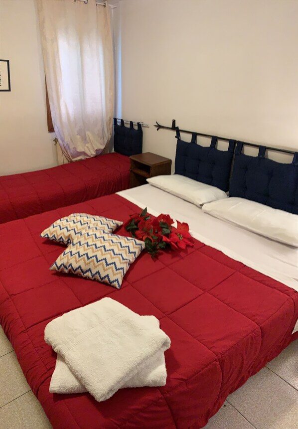 Una habitación de hotel con una colcha roja, dos almohadas con un estampado en zigzag, una toalla blanca y un ramo de flores rojas.