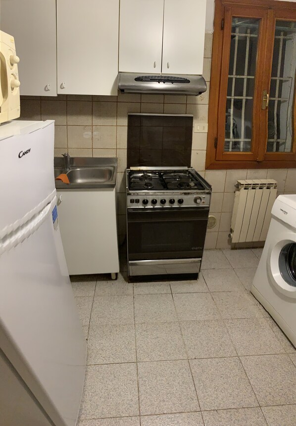 Una cocina compacta con estufa a gas, horno empotrado, pileta y lavadora.