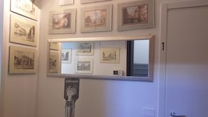 A hallway with framed black and white photographs on the walls, a mirror reflecting the room, and a hand sanitizer dispenser. - B&B San Vitale (Bologna)