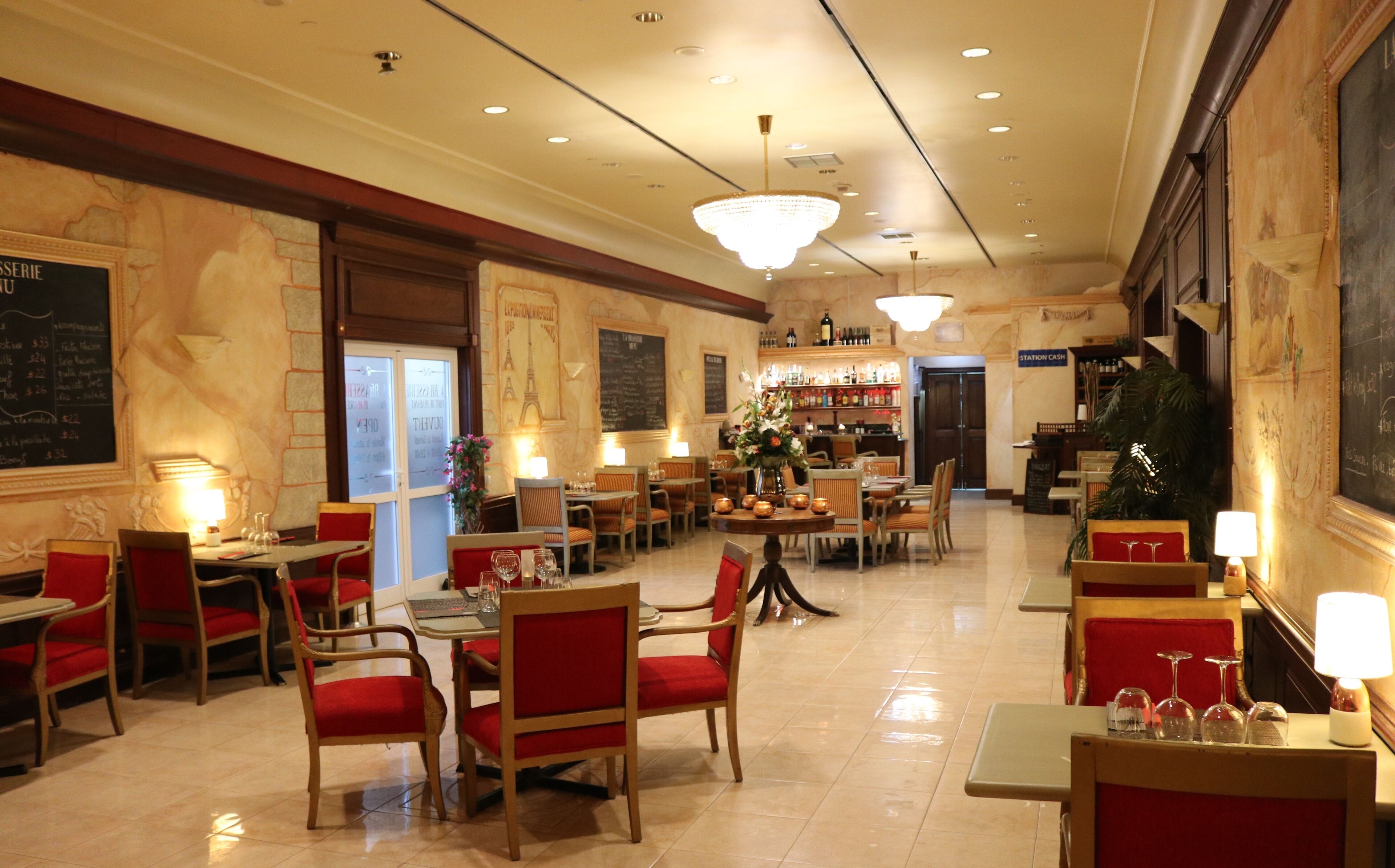 Un restaurant avec de nombreuses tables et chaises, un bar avec des bouteilles exposées et un lustre.