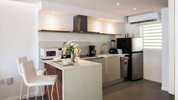 Una cocina moderna con una isla central, taburetes de bar blancos, microondas, cafetera, licuadora y refrigerador.