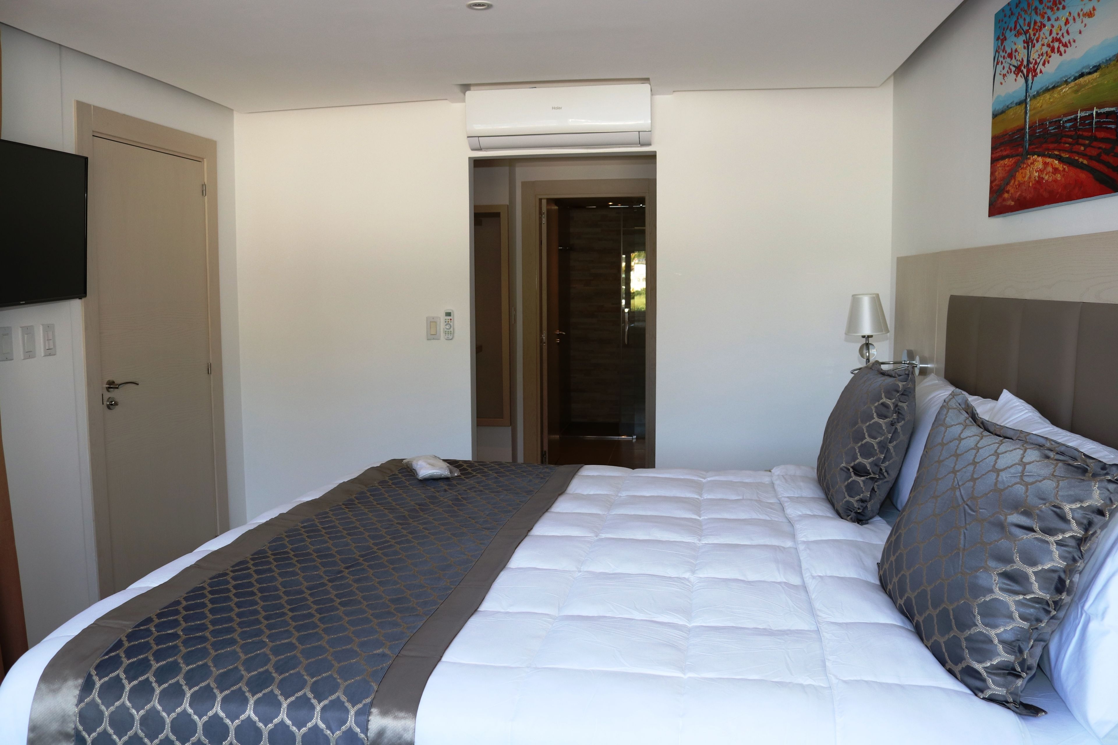 A hotel room with a bed, a television, a painting, and a door.