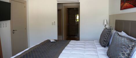 A hotel room with a bed, a television, a painting, and a door.