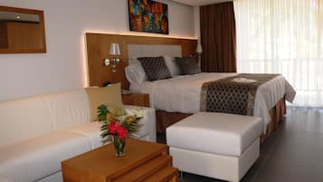 A modern hotel room with a large bed, a sofa, a wooden side table, and a vase of flowers.