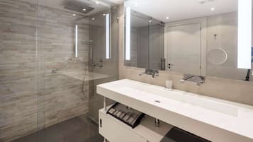 A modern bathroom with a glass-enclosed shower, a white vanity with a large mirror, and a built-in storage drawer.