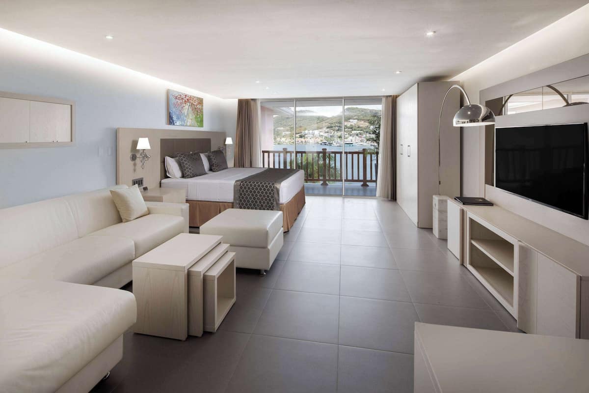 Una habitación de hotel moderna con cama, sofá, televisor y balcón con vistas.