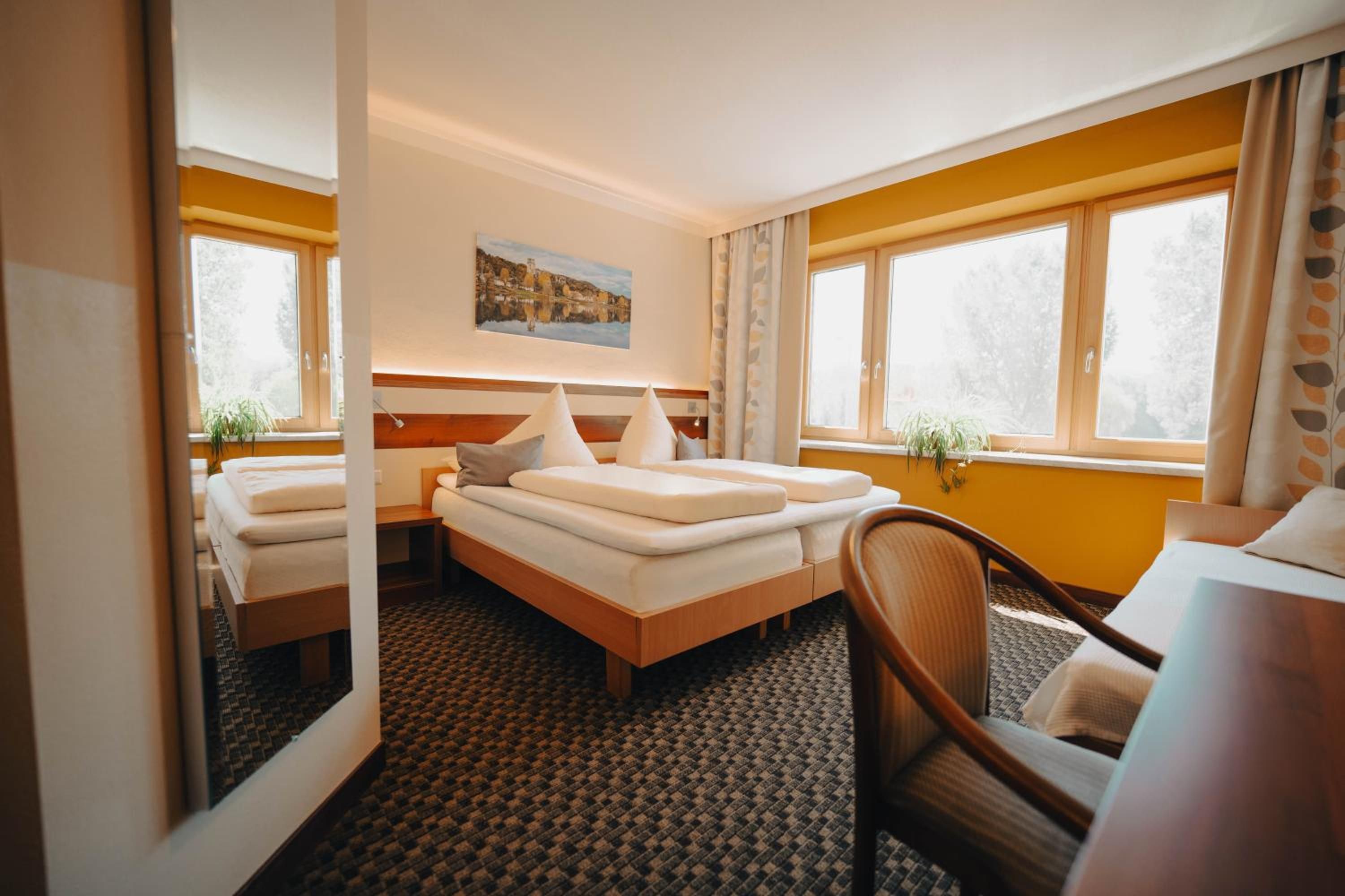 Habitación de hotel con cama, escritorio y silla. Hay un cuadro en la pared y una ventana con cortinas.