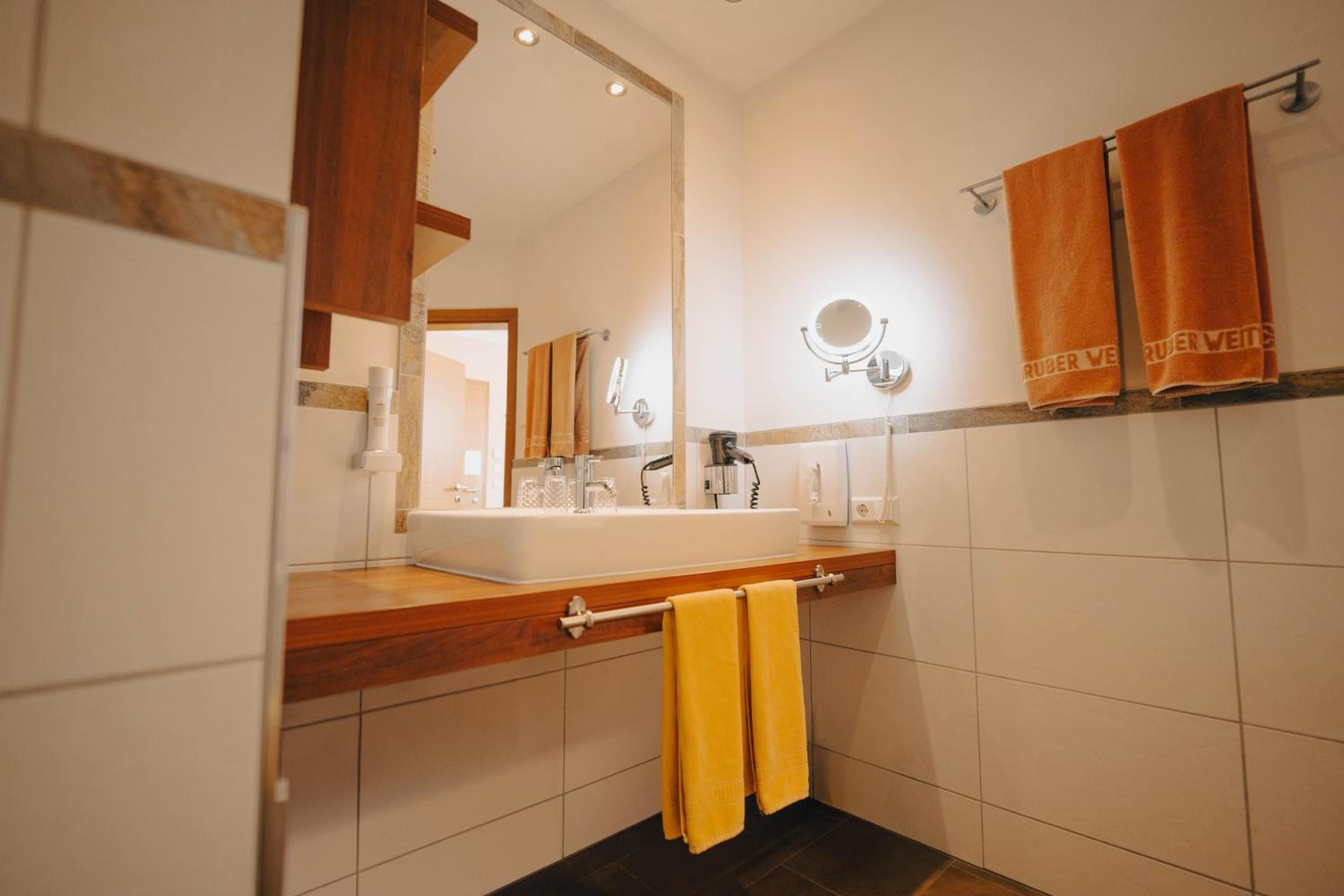 Een badkamer met een houten wastafelmeubel, een spiegel, een handdoekrek met handdoeken en een wastafel met kraan.