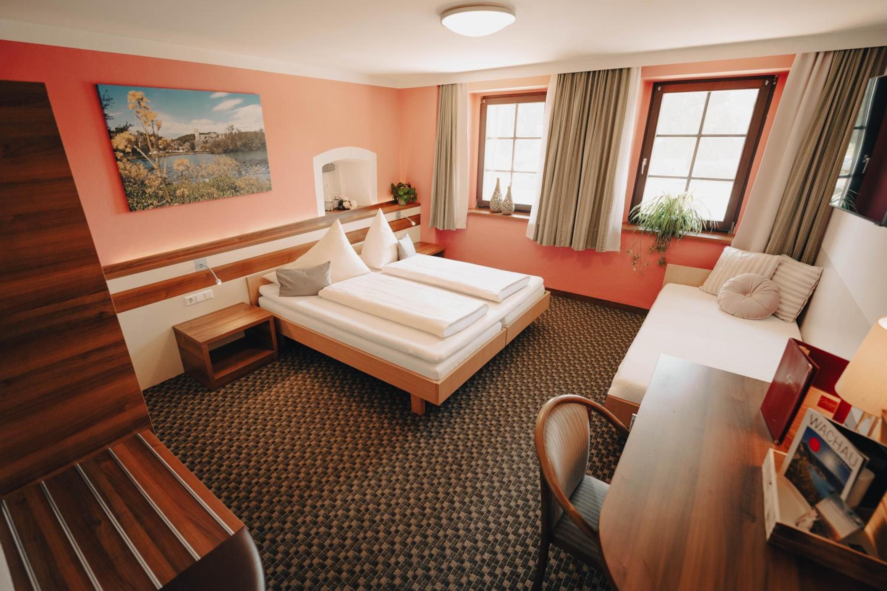 Een hotelkamer met een bed, een bureau, een stoel, een raam met gordijnen en een schilderij aan de muur.