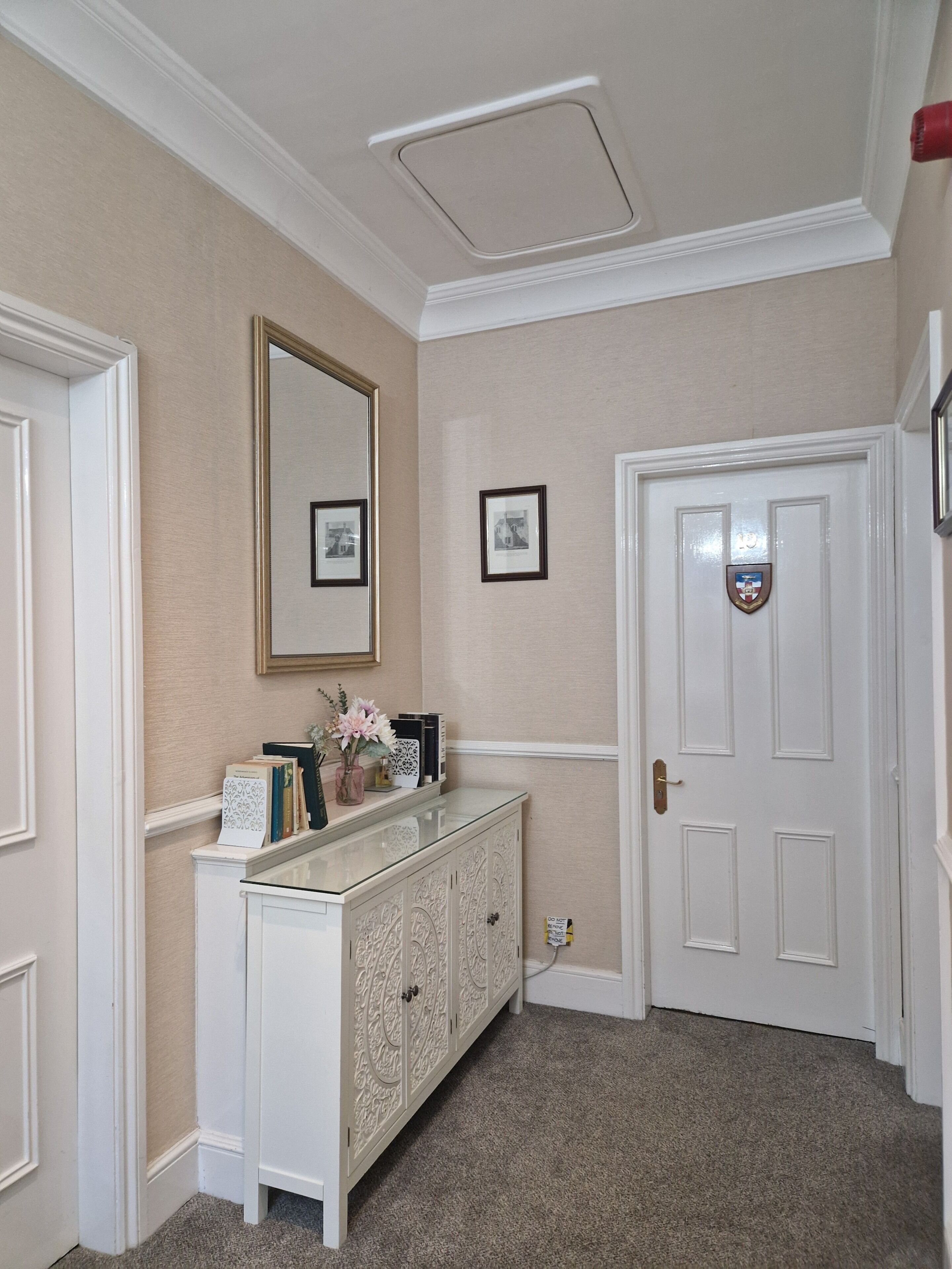 Un pasillo con una puerta blanca, una consola blanca con objetos decorativos y cuadros en la pared.