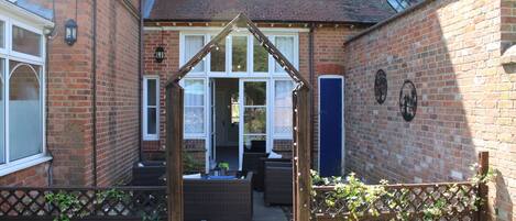 A courtyard with a wooden archway, wicker furniture, and a brick building with windows.