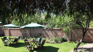 Un patio con muro de ladrillo, césped verde y mobiliario de madera bajo sombrillas.