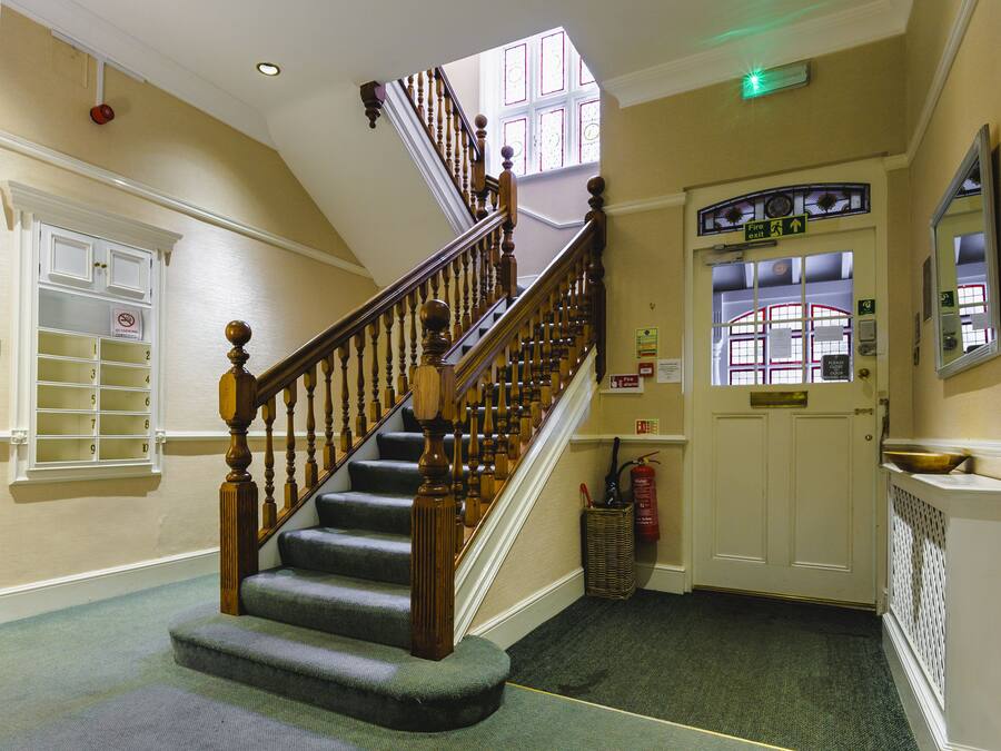 A staircase with wooden balusters, carpeted steps, and a fire exit sign.