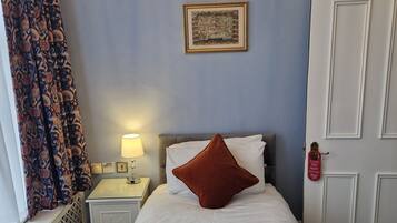 Une chambre d’hôtel avec un lit, une table de chevet avec une lampe, un tableau encadré au mur et une porte avec une pancarte.