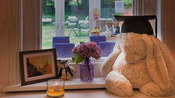 A window sill with a framed picture, a candle, a vase with flowers, and a stuffed bunny wearing a graduation cap.