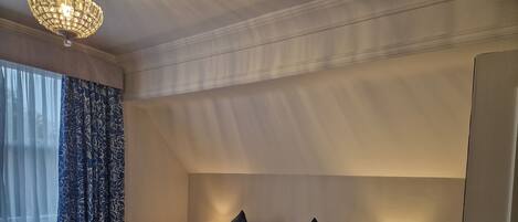 A hotel room with a neatly made bed, a nightstand with a lamp, and a window with curtains.