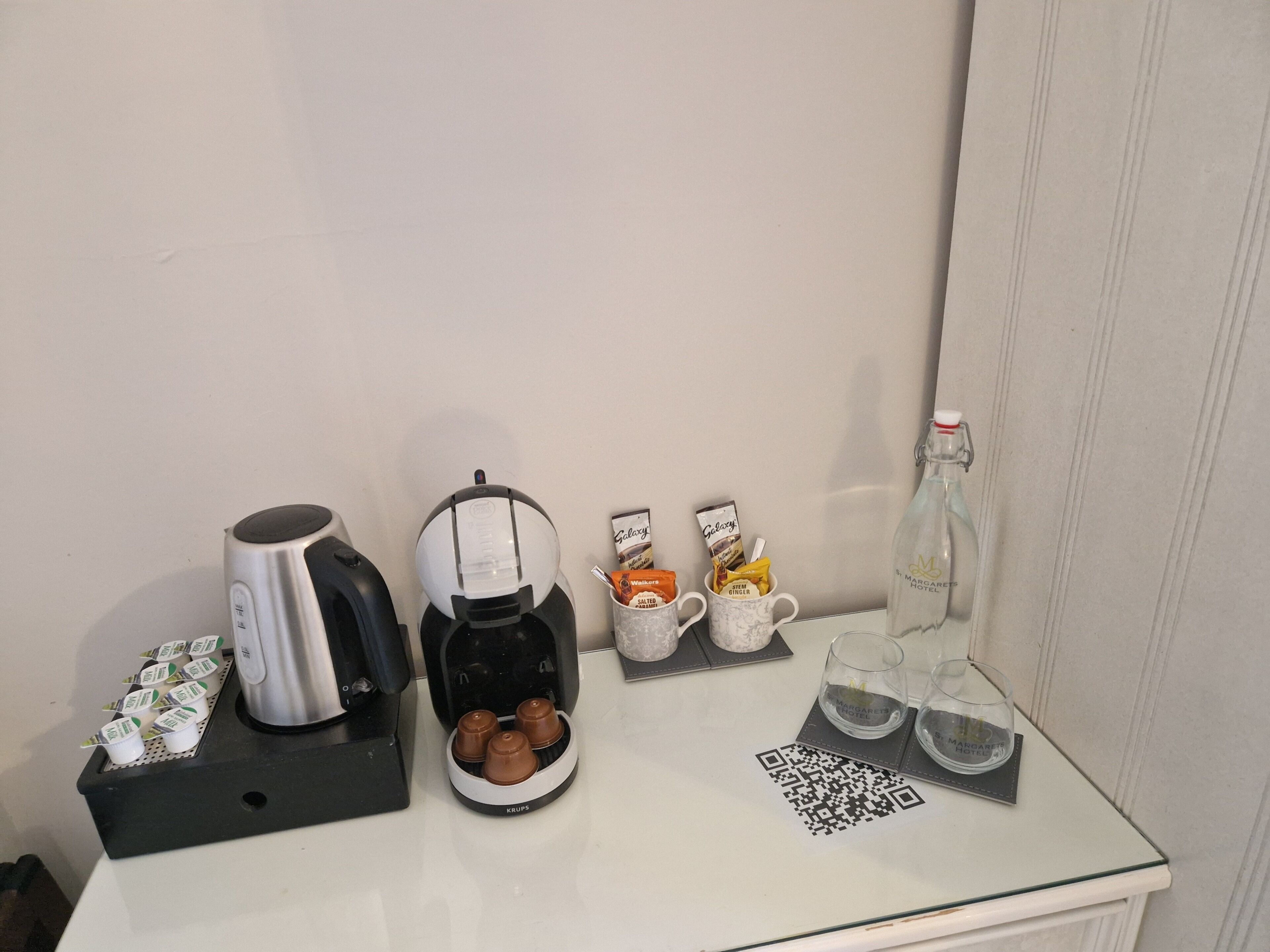 A coffee station with a coffee maker, a Krups coffee dispenser, and a mug with a QR code.