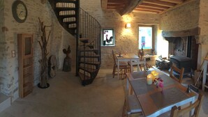 Interior rústic amb una escala espirall, parets de pedra, taula de dinar de fusta i flassons, i una llar de foc.