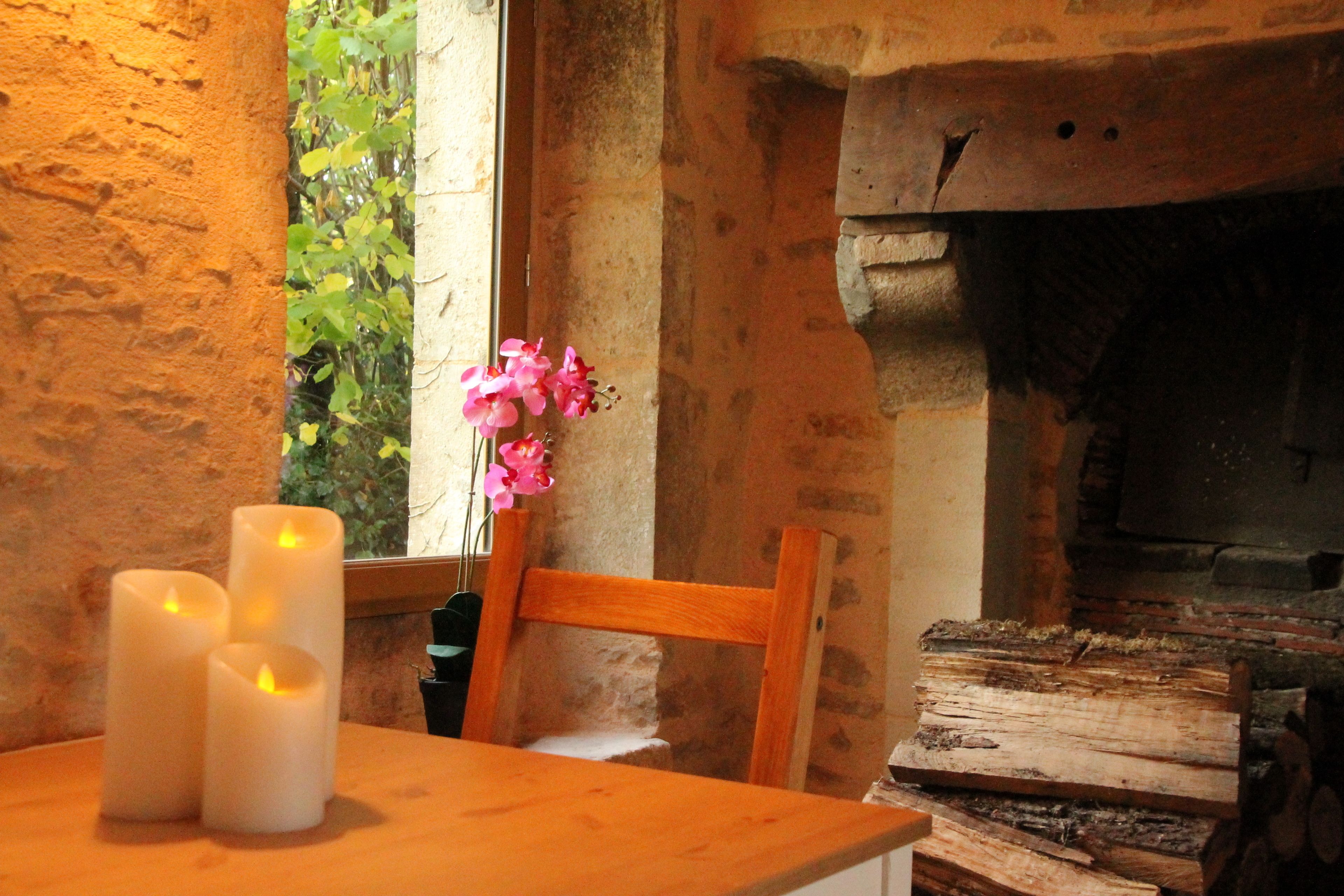 A rustic room with a wooden table, three lit candles, and a wooden chair.