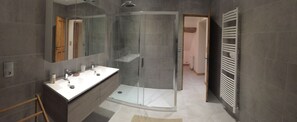 Un baño moderno con ducha de vidrio, tocador con espejo y perchero para toallas.