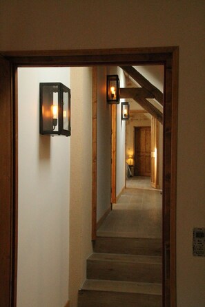 Un couloir avec des marches en bois et deux lampes fixées au mur.