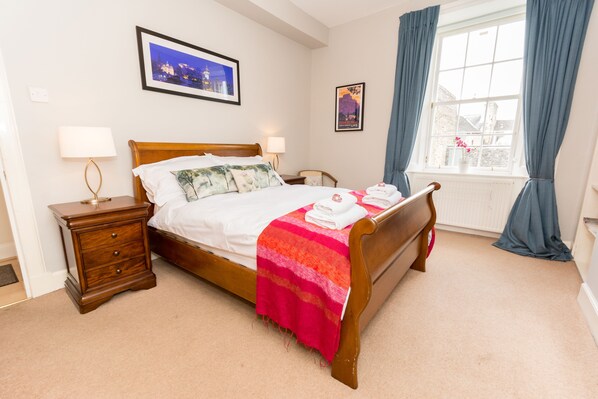 A neatly made bed with a striped blanket, a wooden nightstand with a lamp, and a window with curtains.