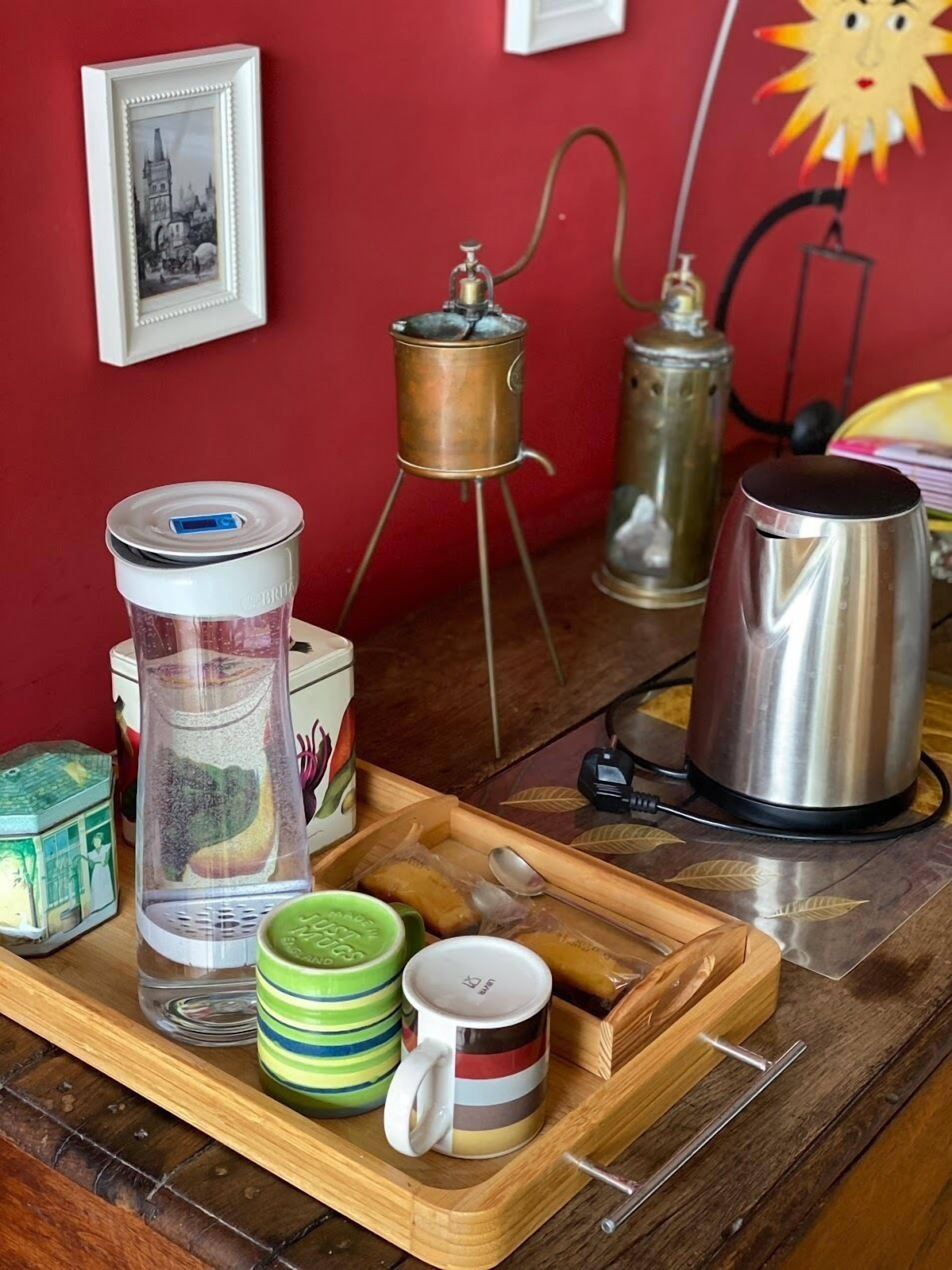 A kitchen counter with a coffee maker, a kettle, a teapot, and a tray with cups and a water container.
