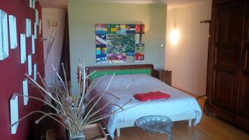 A bedroom with a bed, a nightstand, a chair, a wall with artwork, and a wooden door.