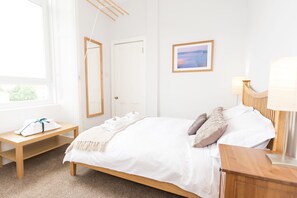 A neatly arranged bedroom with a bed, bedside table, lamp, and a framed picture on the wall. - Beautiful City Center 2 Bed Apartment with Park View (Edinburgh)