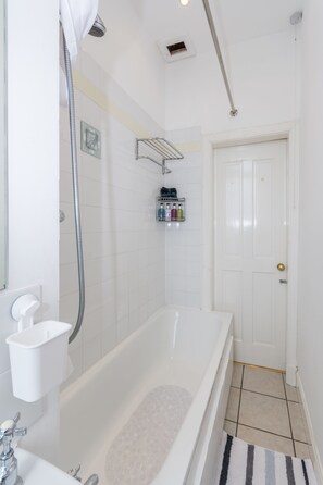 A bathroom with a bathtub, a shower, and a toilet. There is a towel rack and a shelf with toiletries. - Beautiful City Center 2 Bed Apartment with Park View (Edinburgh)