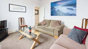 Ein Wohnzimmer mit einem Glastisch, einem beigefarbenen Sofa, einem pinkfarbenen Sofa und einem Fernseher.