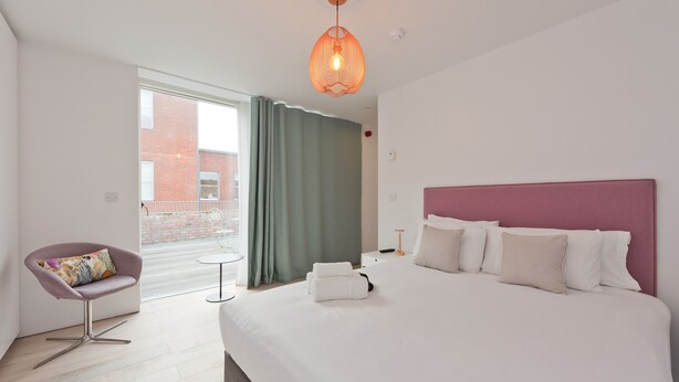 A hotel room with a large bed, a chair, a small table, and a view of a building outside. - Double Penthouse en suite - hiphipstay (Dublin)