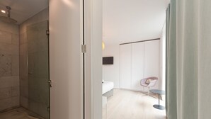 A modern bathroom with a glass shower enclosure, a white toilet, and a small bedside table with a chair. - Double Penthouse en suite - hiphipstay (Dublin)