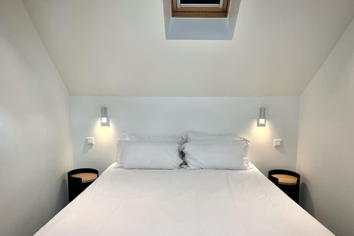 A bedroom with a large bed, two bedside tables, and a skylight above.