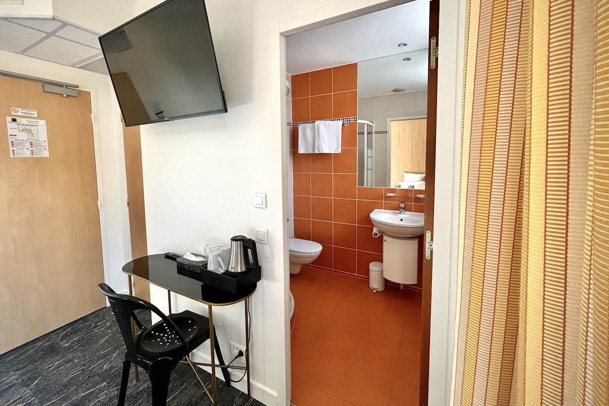 A compact hotel room with a kitchenette, a single bed, and a bathroom with orange tiles.