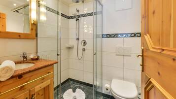 A bathroom with a glass shower enclosure, a white toilet, and a wooden vanity with a marble countertop.