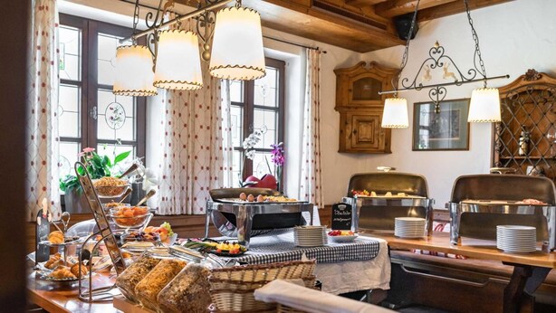 A buffet setup with various food items, including pastries, fruits, and a hot dish, in a room with wooden furniture and decorative elements. - Landgasthof zum Erdinger Weissbrau (Rosenheim)