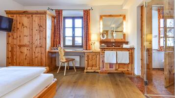 A wooden-furnished bedroom with a bed, desk, chair, and a large mirror.