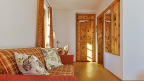 A cozy living room with a red sofa, floral cushions, a wooden door, and a wooden floor. - Landgasthof zum Erdinger Weissbrau (Rosenheim)