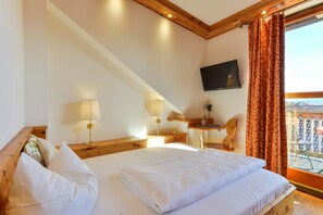 A bedroom with a large bed, wooden headboard, a flat-screen TV, a small table with a lamp, and a window with curtains. - Landgasthof zum Erdinger Weissbrau (Rosenheim)