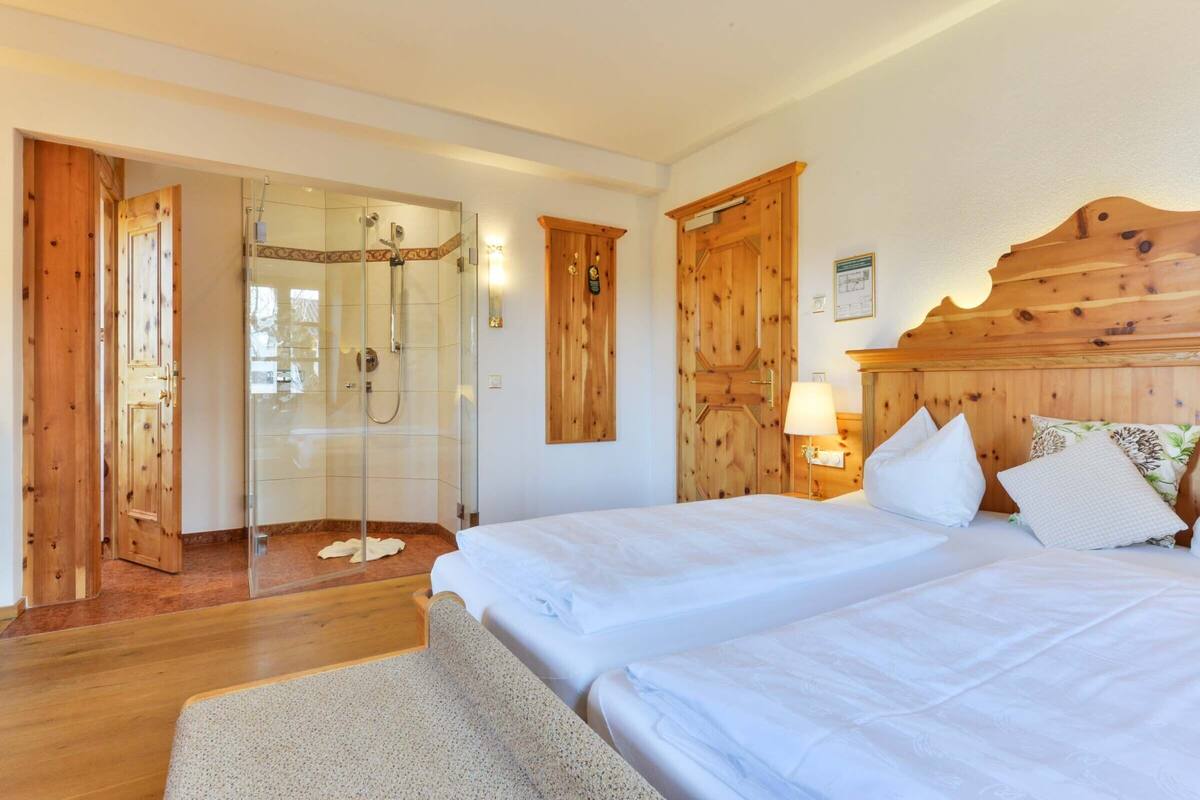 Ein Hotelzimmer mit Holztüren, einer Duschkabine, zwei Betten mit weißen Laken und einem hölzernen Kopfteil.