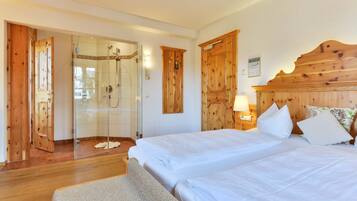 A hotel room with wooden doors, a shower area, two beds with white linens, and a wooden headboard.