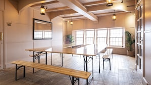 A spacious room with wooden floors, large windows, and multiple tables and benches.