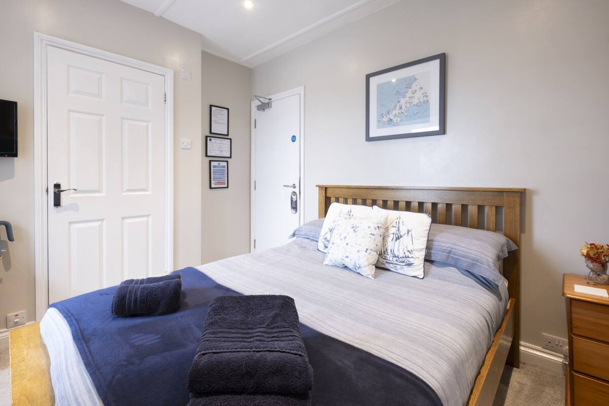 A bedroom with a bed, a wooden headboard, a bedside table, a wall-mounted TV, and framed certificates on the wall.